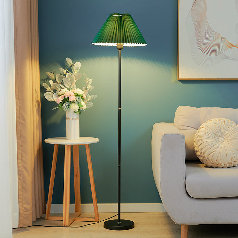 Stehlampe mit grünem Faltenschirm neben Sofa und Holztisch

