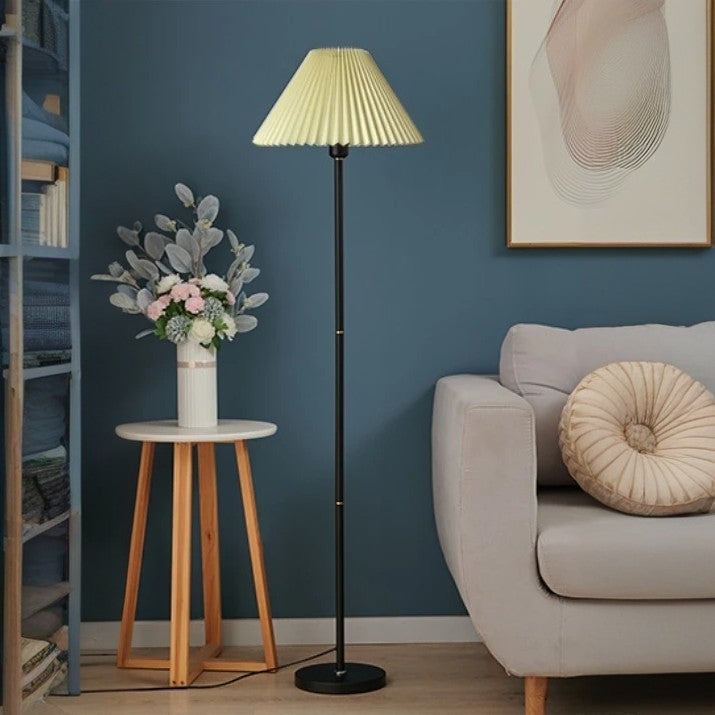 Schwarze Stehlampe mit Faltenlampenschirm, warm beleuchtet neben hellem Sofa
